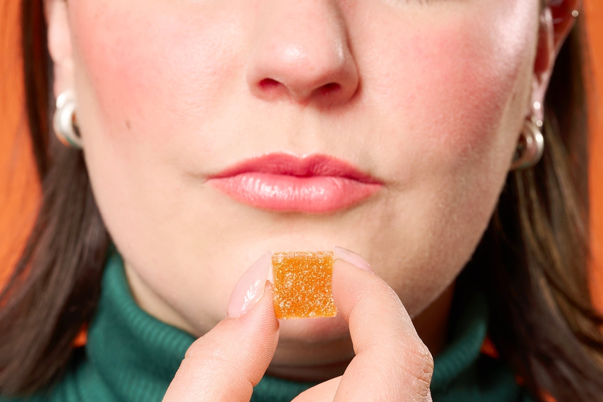 a woman holding an orange THC gummy to her mouth