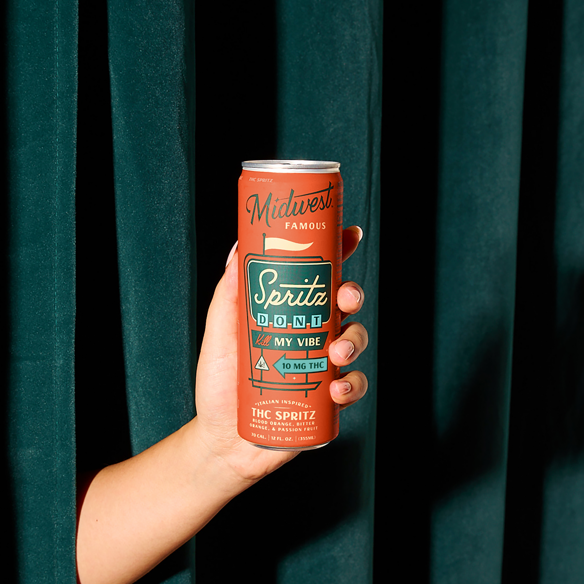 an arm holding a 10mg thc spritz can in front of a dark green curtain