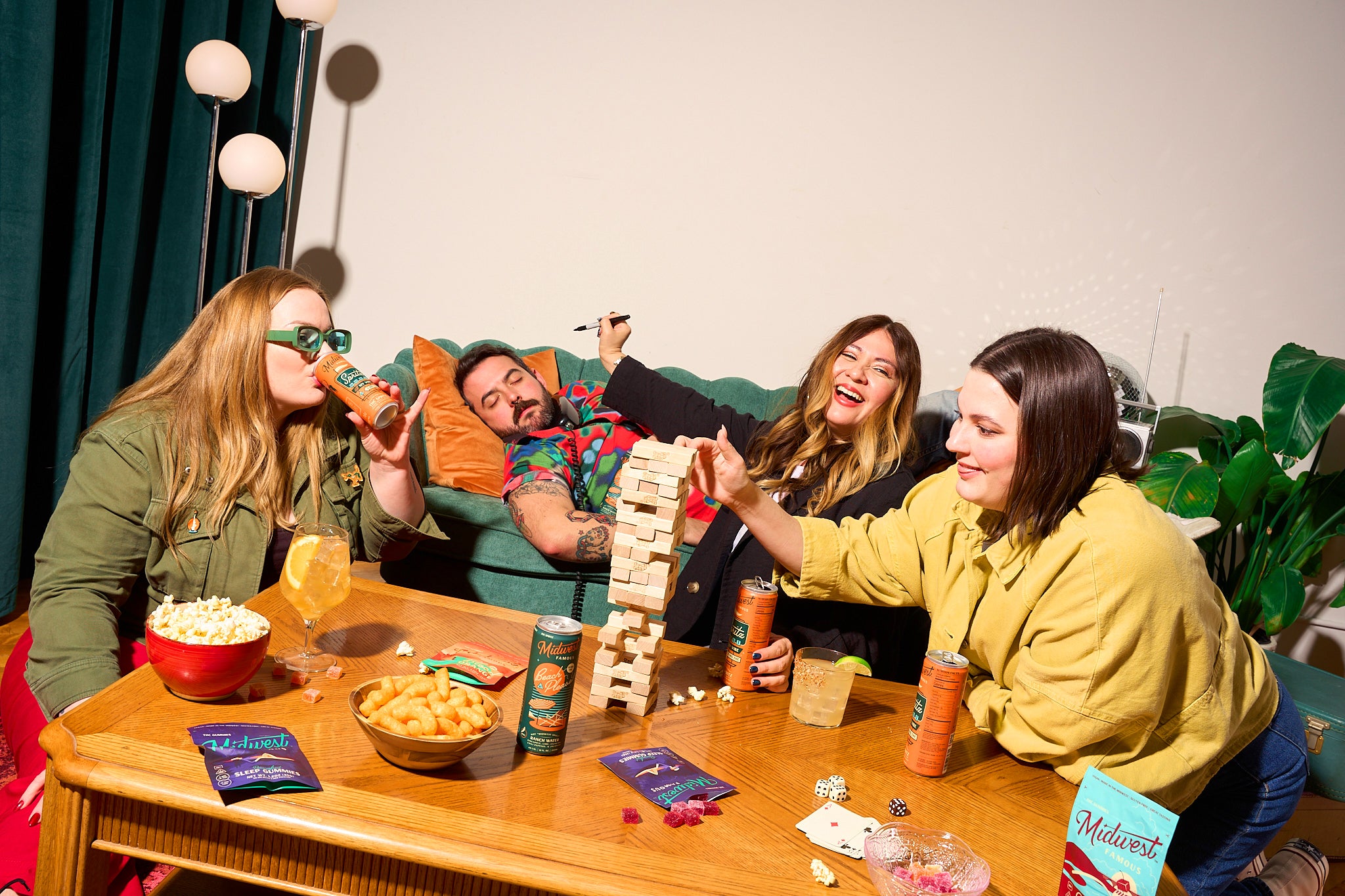 a group of people laughing at a tabletop while drinking orange cans