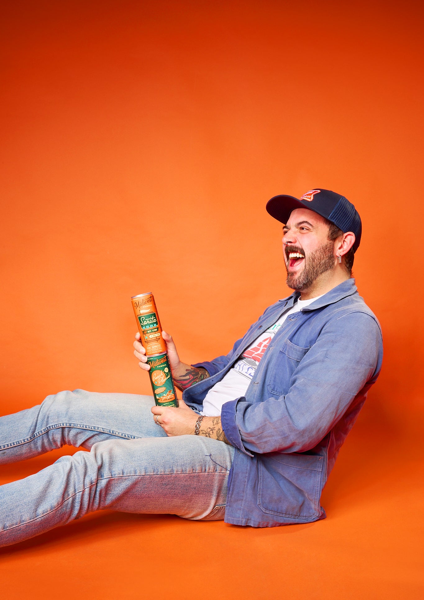 a man sitting in front of an orange background from the side while holding two stacked thc drink cans
