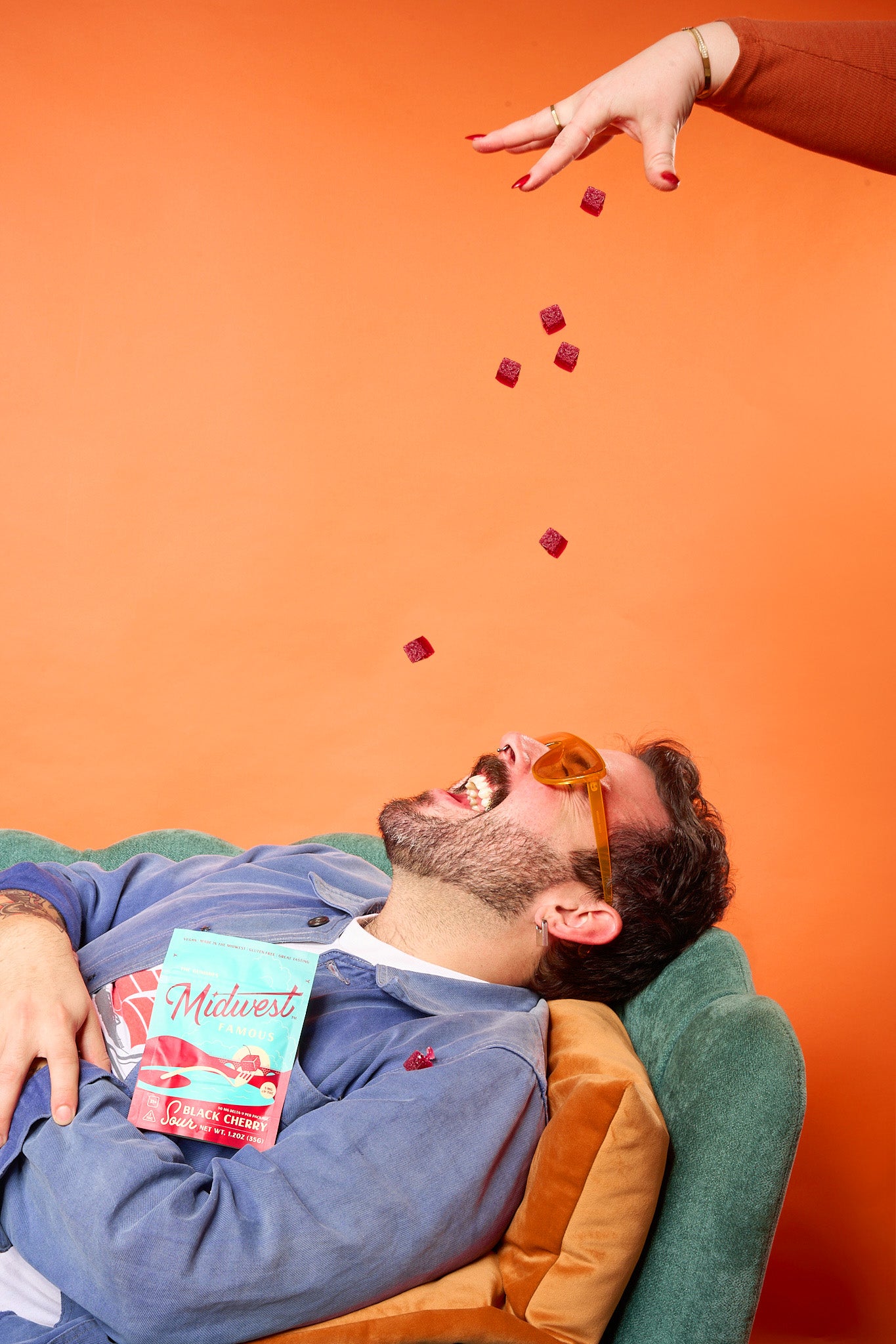 a man laying in front of an orange background with his mouth open trying to catch thc gummies falling from above