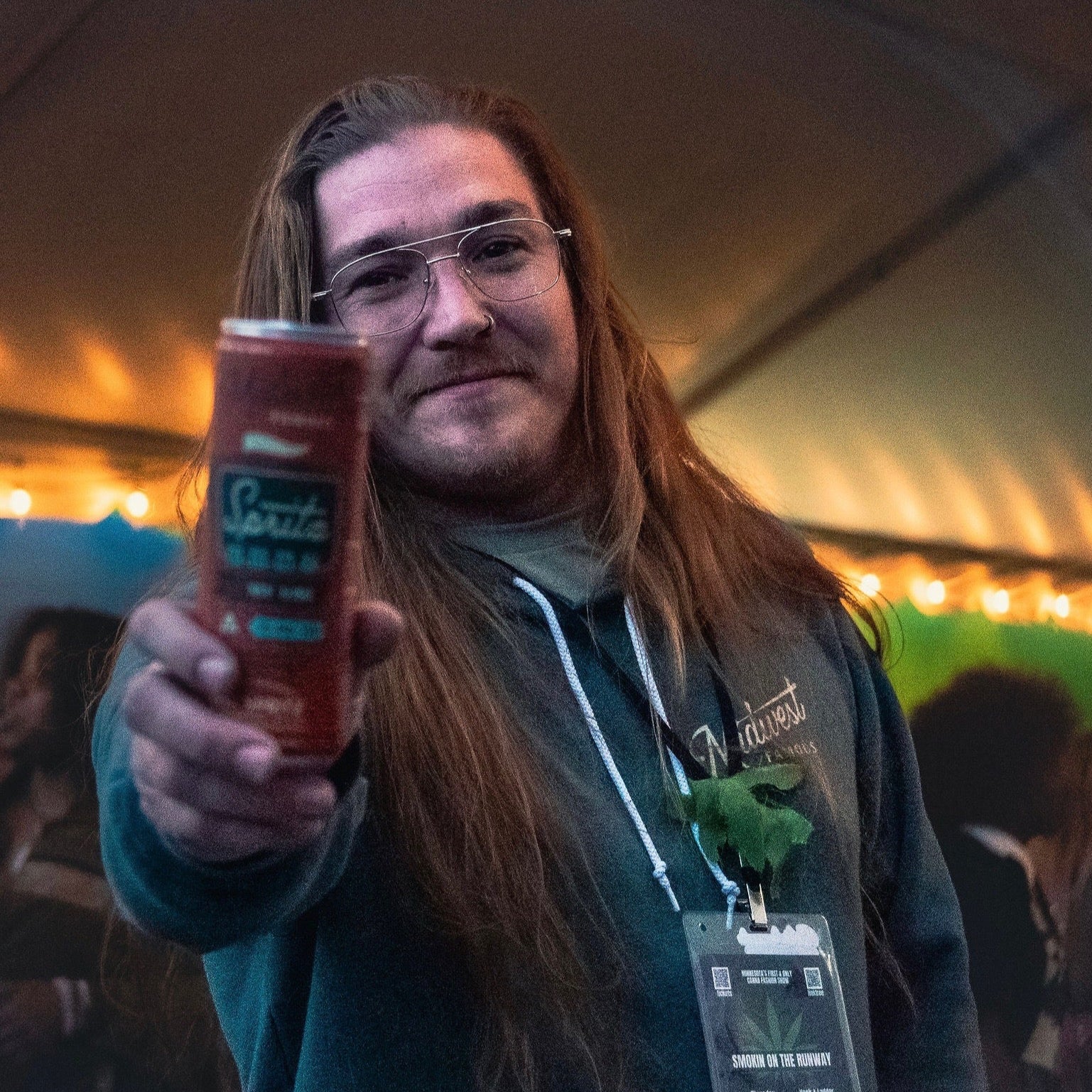 a man with long hair holding a orange thc can to the camera