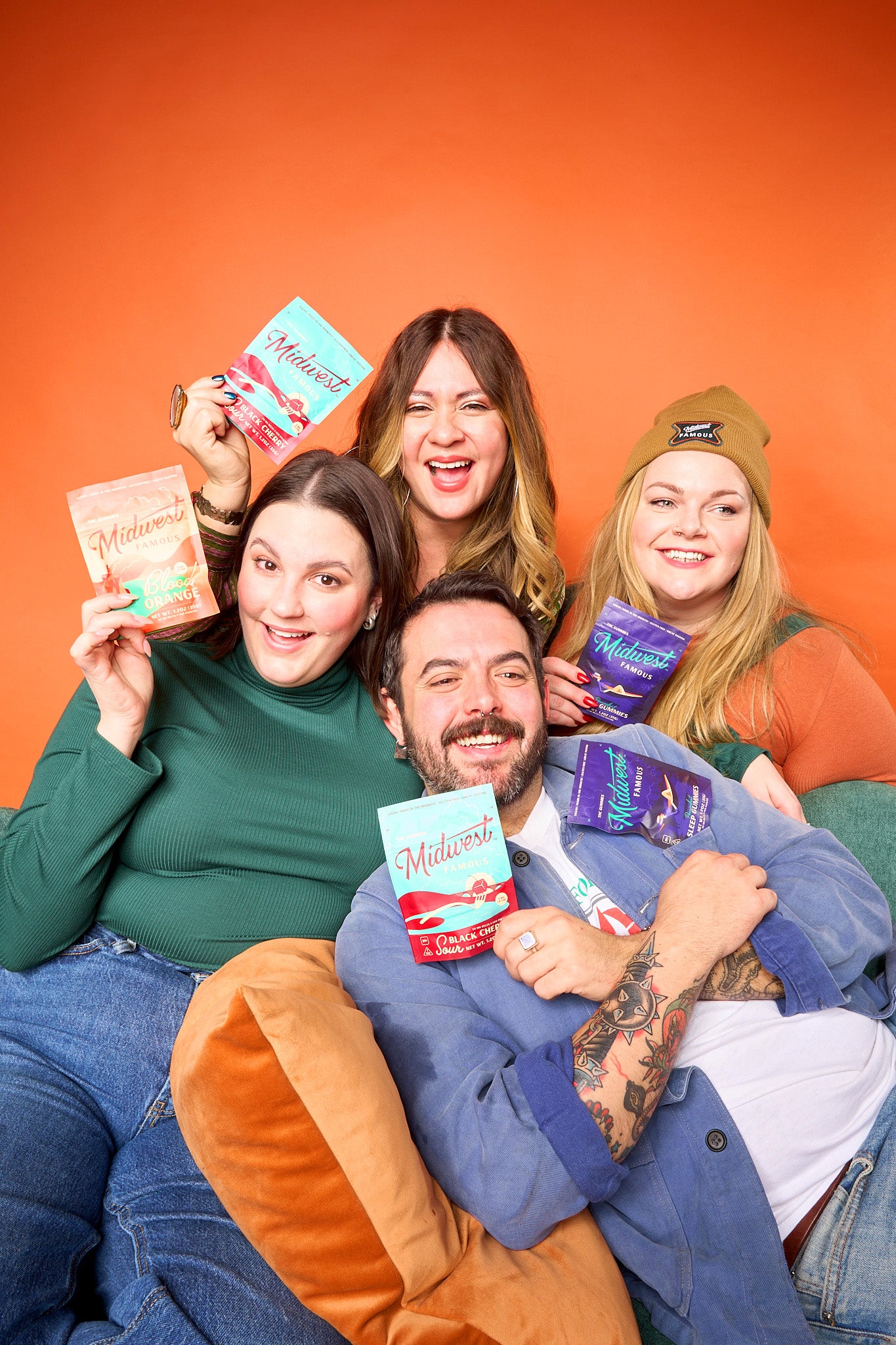 a group of people posing in front of an orange background with multiple bags of midwest famous thc gummies